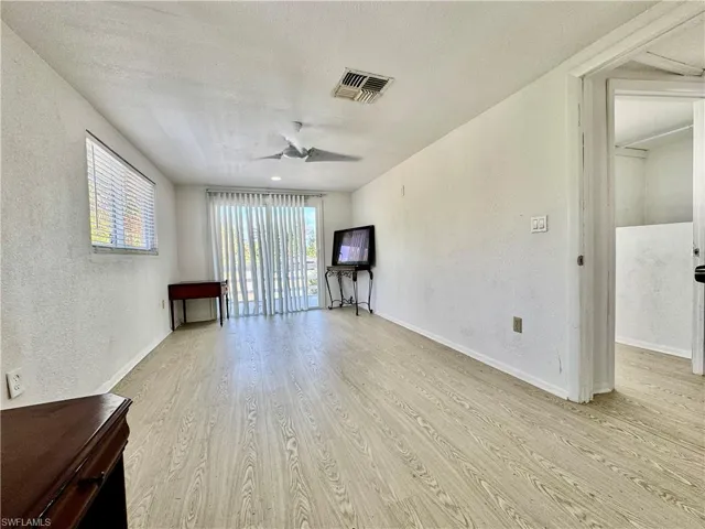 Unfurnished living room featuring a textured wall, light wood-style flooring, a ceiling fan, and a textured ceiling