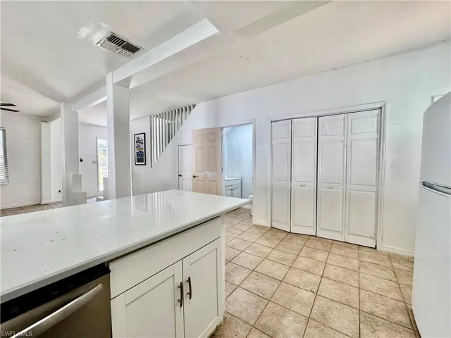 Kitchen featuring white cabinets, freestanding refrigerator, stainless steel dishwasher, light stone counters, and light tile patterned floors