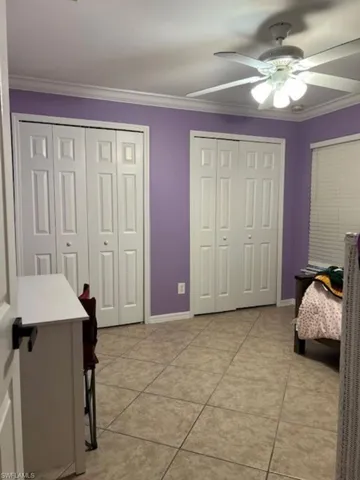 Bedroom featuring multiple closets, light tile patterned floors, ornamental molding, ceiling fan, and baseboards