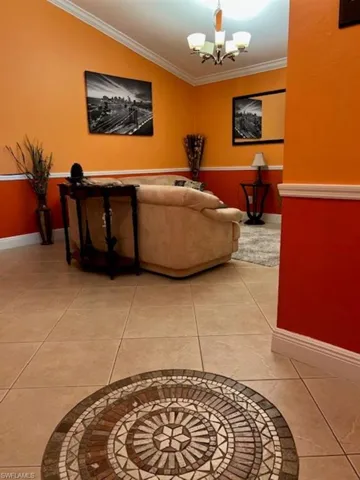 Living room with light tile patterned flooring, crown molding, a chandelier, and baseboards