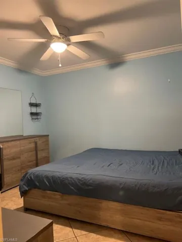 Bedroom with ornamental molding, light tile patterned floors, and a ceiling fan