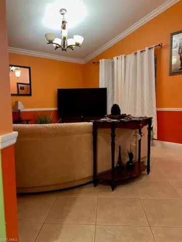 Living room featuring light tile patterned flooring, ornamental molding, and a chandelier