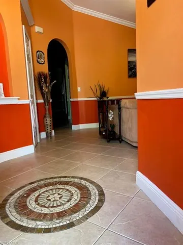 Corridor with arched walkways, crown molding, baseboards, and tile patterned flooring