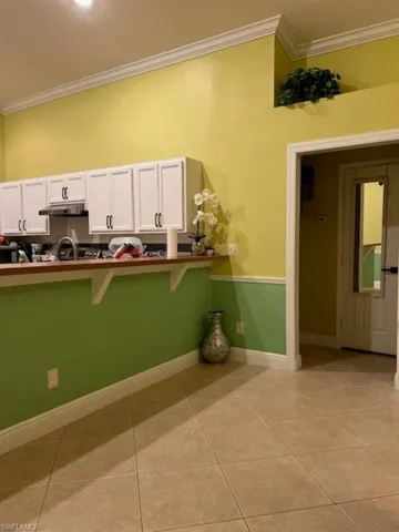 Kitchen featuring ornamental molding, white cabinetry, a breakfast bar, light tile patterned floors, and extractor fan
