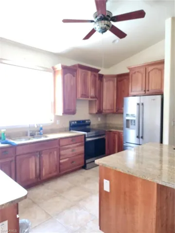 Kitchen with refrigerator, range, ceiling fan, lofted ceiling, and wood finish cabinetry