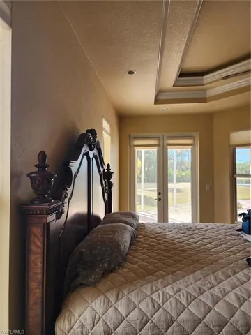 Bedroom with french doors, access to exterior, a textured ceiling, ornamental molding, and a raised ceiling