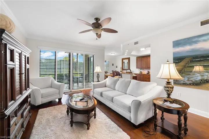 Living room featuring crown molding, dark wood-style flooring, and ceiling fan