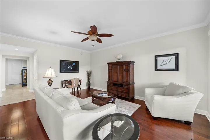 Living room with ornamental molding, dark wood-style floors, and a ceiling fan