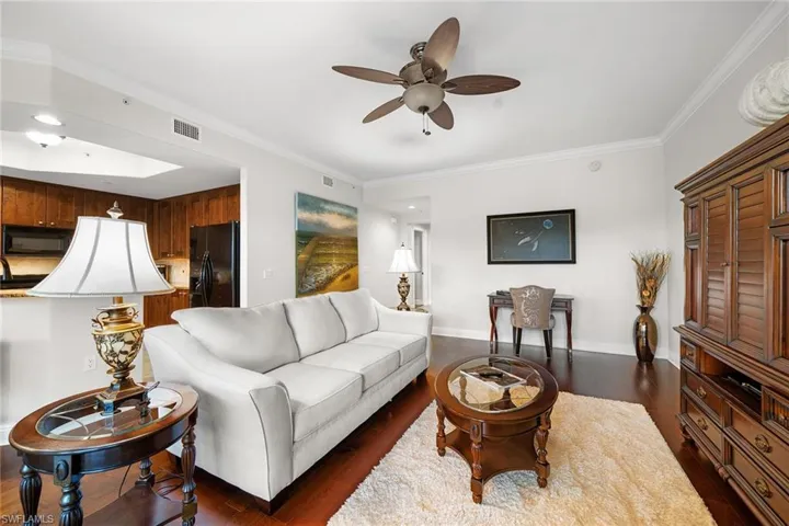 Living area with dark wood-type flooring, ornamental molding, and a ceiling fan