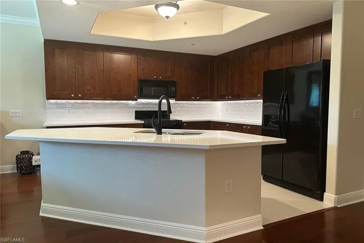 Kitchen featuring black appliances, dark brown cabinetry, a kitchen island with sink, light wood-style flooring, and decorative backsplash