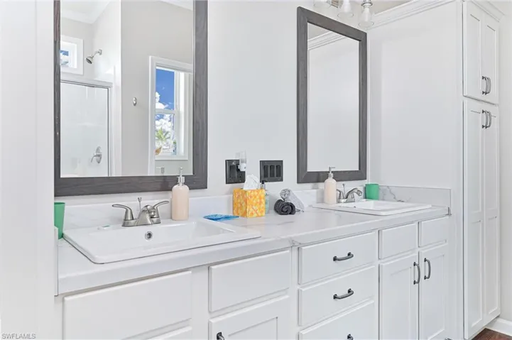 Bathroom featuring plenty of natural light, a stall shower, crown molding, and double vanity