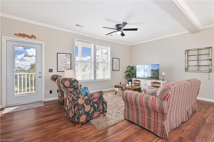 Living room with crown molding, dark wood-type flooring, and a ceiling fan