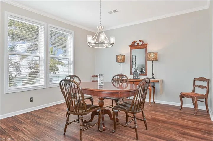 Dining room with dark wood-type flooring, crown molding, and a chandelier