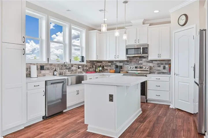 Kitchen with light countertops, appliances with stainless steel finishes, white cabinetry, crown molding, and decorative light fixtures