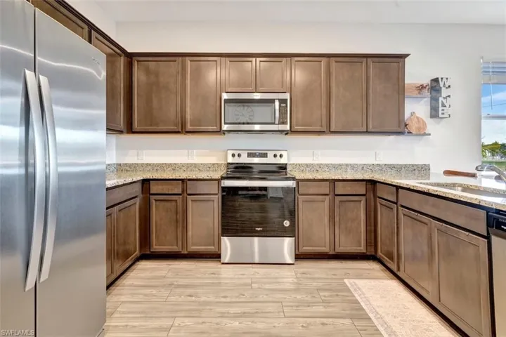 Kitchen with stainless steel appliances, light stone counters, light wood-style floors, and dark brown cabinetry