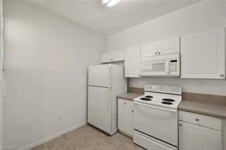 Kitchen featuring light tile patterned floors, white cabinets, white appliances, and baseboards