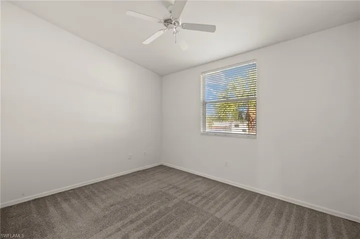 Spare room with a ceiling fan, baseboards, and dark colored carpet