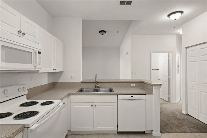 Kitchen featuring visible vents, a peninsula, white appliances, white cabinetry, and a sink