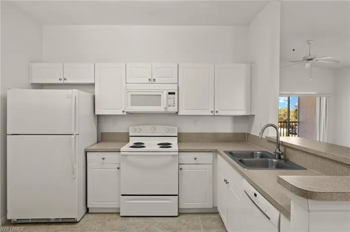 Kitchen featuring a ceiling fan, a sink, white appliances, a peninsula, and white cabinets