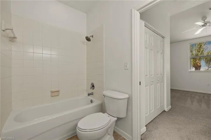 Bathroom featuring baseboards, toilet,  shower combination, and a ceiling fan