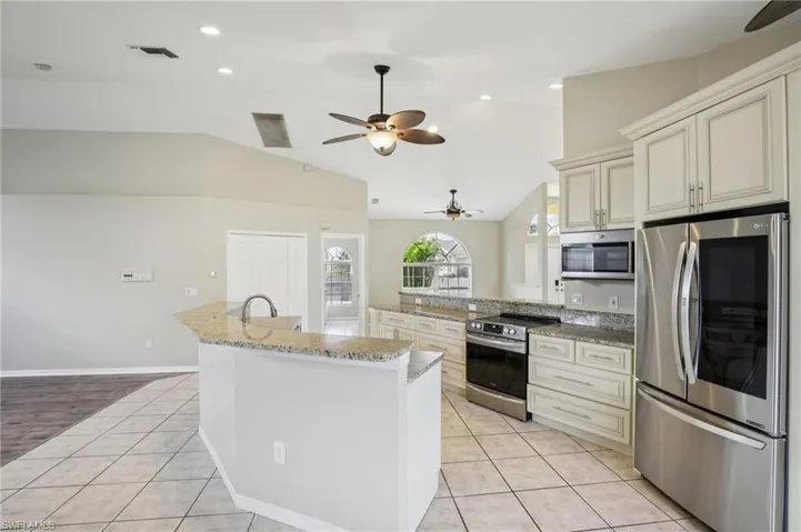 Kitchen with light tile patterned flooring, stainless steel appliances, a ceiling fan, vaulted ceiling, and light stone counters