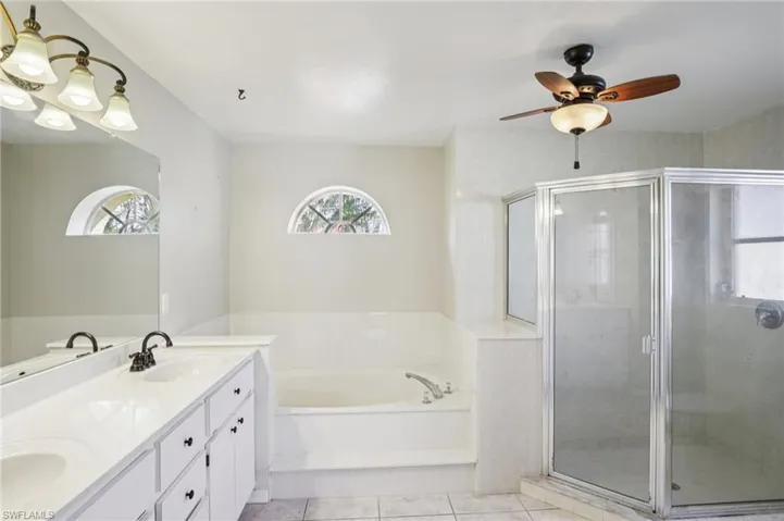 Bathroom featuring double vanity, a shower stall, a bath, ceiling fan, and healthy amount of natural light