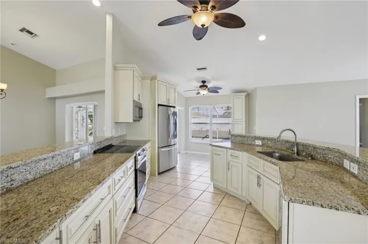 Kitchen with stainless steel appliances, light stone counters, ceiling fan, white cabinetry, and recessed lighting