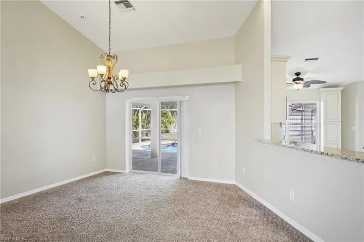 Carpeted spare room featuring lofted ceiling, hanging lights, and ceiling fan