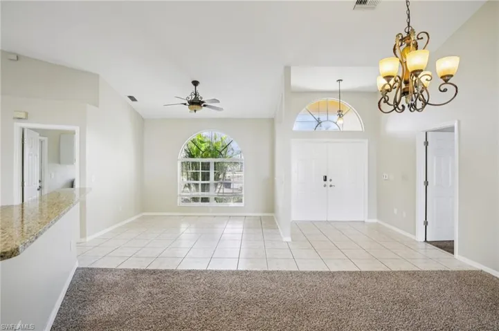 Entryway featuring a chandelier, a ceiling fan, light tile patterned floors, light carpet, and lofted ceiling