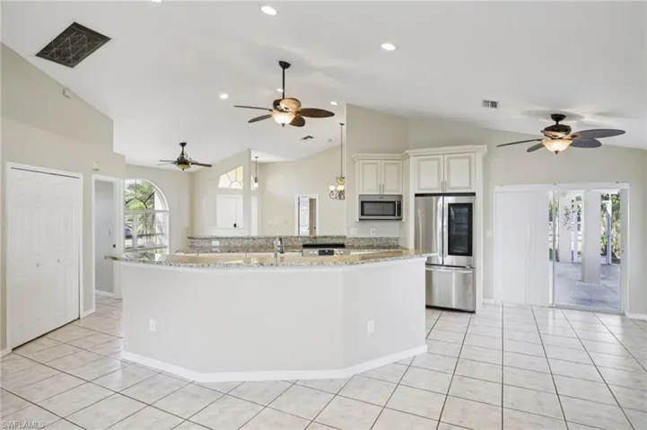 Kitchen with a ceiling fan, stainless steel appliances, light stone counters, decorative light fixtures, and lofted ceiling