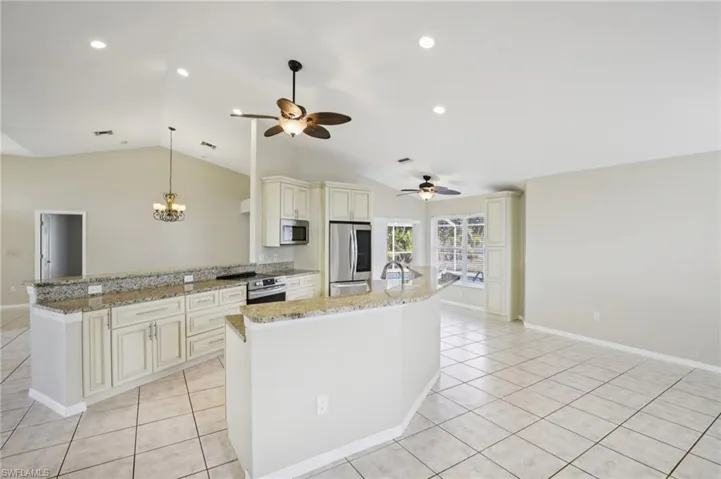 Kitchen featuring cream cabinets, hanging lights, light stone countertops, stainless steel appliances, and a kitchen island with sink