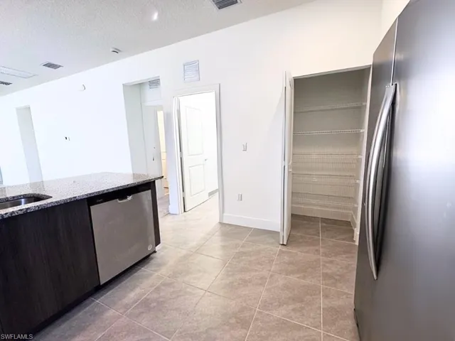 Kitchen with stainless steel appliances, light stone countertops, a textured ceiling, dark brown cabinetry, and light tile patterned floors