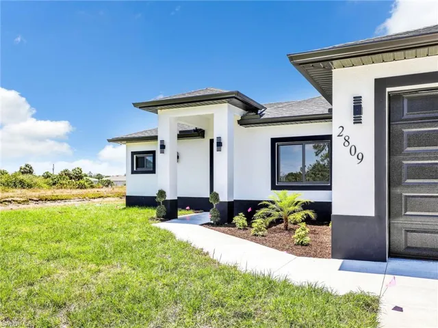 Doorway to property with a lawn, roof with shingles, and stucco siding