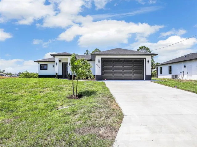 Prairie-style house featuring a front lawn, a garage, central AC unit, driveway, and stucco siding