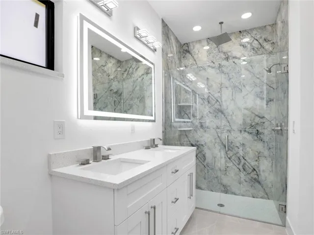 Full bathroom featuring recessed lighting, a marble finish shower, a sink, and double vanity
