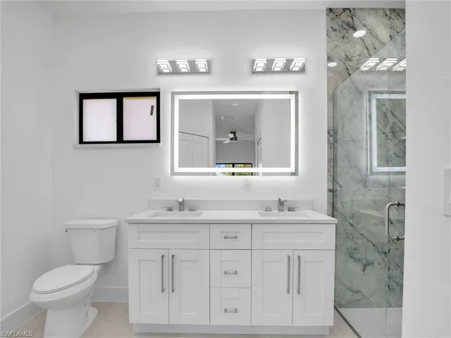 Bathroom with toilet, baseboards, a marble finish shower, and a sink