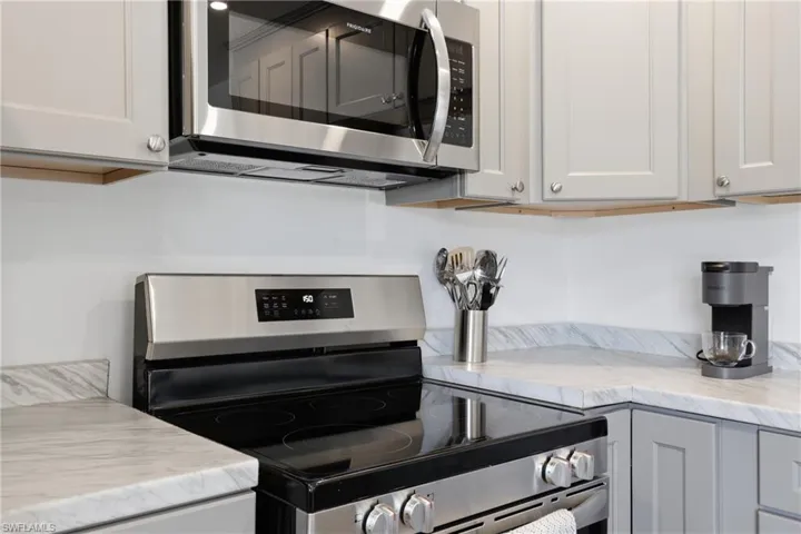 Kitchen featuring stainless steel appliances, light stone counters, and gray cabinets