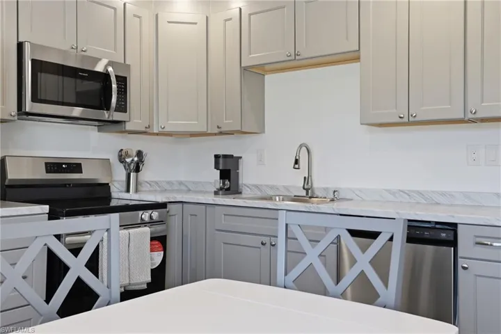 Kitchen featuring gray cabinets, stainless steel appliances, and light stone counters