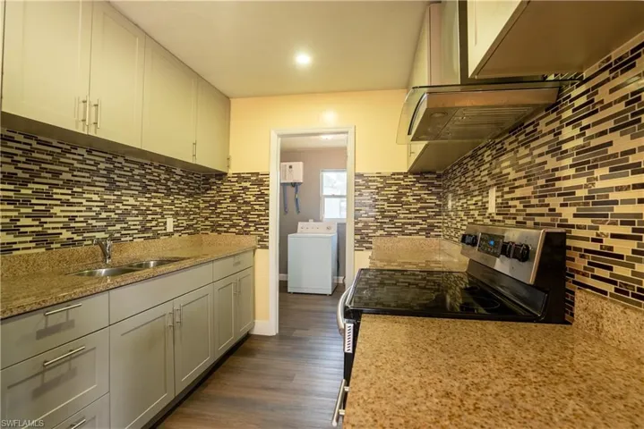 Kitchen with electric stove, washer / clothes dryer, light stone countertops, dark wood-style flooring, and white cabinets