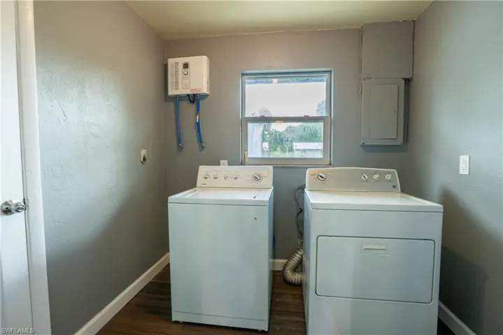 Laundry room with a textured wall, electric panel, dark wood-style floors, washing machine and dryer, and water heater