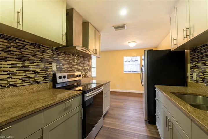 Kitchen featuring stainless steel appliances, tasteful backsplash, light stone counters, extractor fan, and dark wood-style flooring