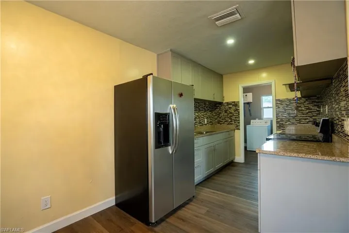 Kitchen featuring stainless steel fridge, dark wood-style flooring, electric range, washer / dryer, and light stone counters