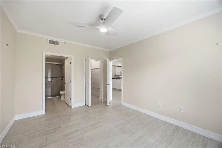 Primary bedroom featuring a walk in closet, crown molding, ceiling fan, ensuite bathroom, and tile flooring