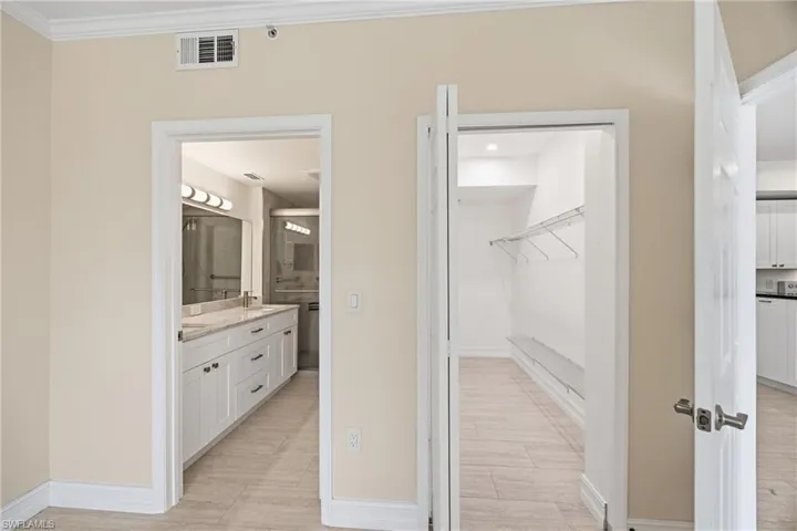 Primary bedroom showing full bath featuring vanity, a walk in closet, crown molding, and tile floors