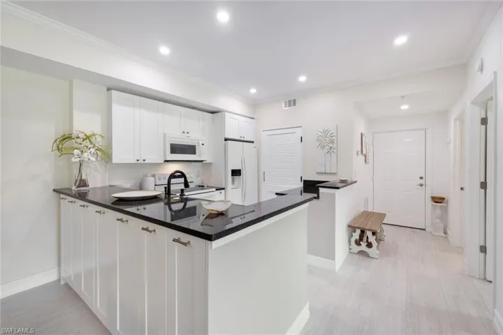 Kitchen with white appliances, white cabinetry, granite countertops and additional cabinet storage on back side of kitchen peninsula