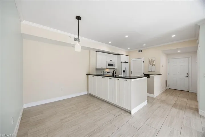 Kitchen with a peninsula, dark countertops, white cabinets, hanging light fixtures, and white appliances