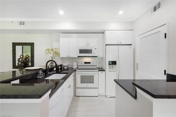 Kitchen with granite countertops, white cabinetry, white appliances, kitchen peninsula, and sink