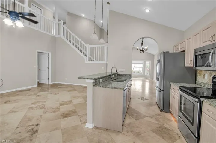 Kitchen with high vaulted ceiling, ceiling fan with notable chandelier, stone countertops, stainless steel appliances, and sink