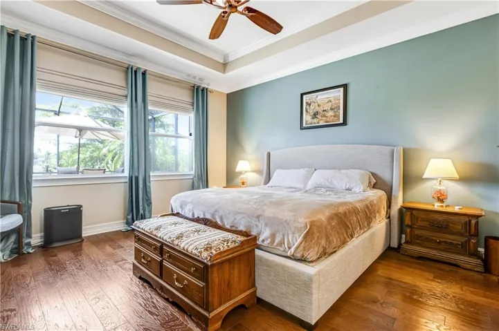 Bedroom with hardwood / wood-style flooring, ornamental molding, a tray ceiling, baseboards, and a ceiling fan