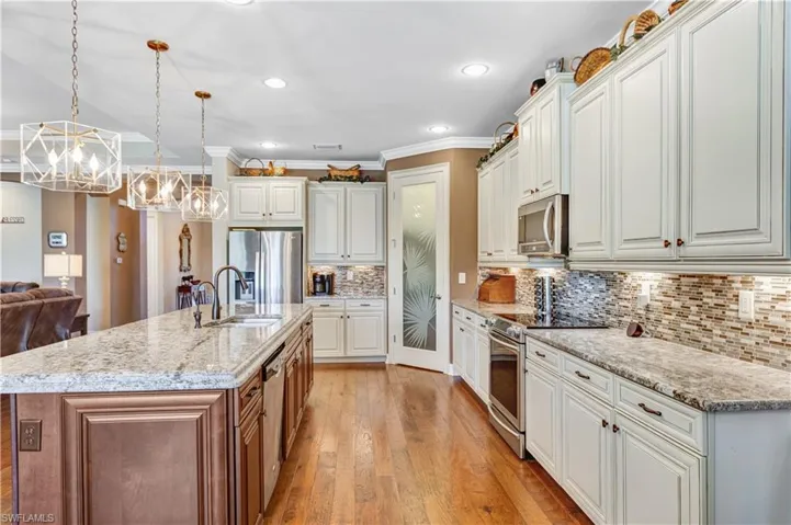 Kitchen with appliances with stainless steel finishes, a sink, a chandelier, light wood-style flooring, and white cabinets